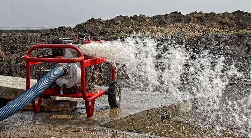 Bomba de água móvel vermelha bombeando água para fora de um canteiro de obras.