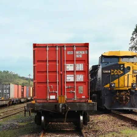 View of the back of a red shipping container on a train car next to a yellow train car in daylight.